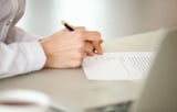 Person writing on document with pen at desk