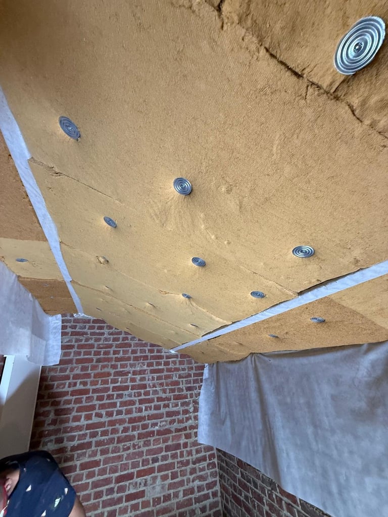 Interior ceiling under construction with drywall, recessed light fixtures, and exposed framing above brick wall