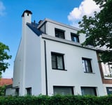 Modern white residential building with dark roof and green surroundings