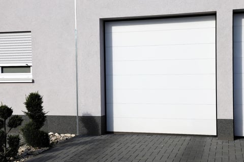 Blank white billboard on modern garage exterior with dark frame and paved driveway