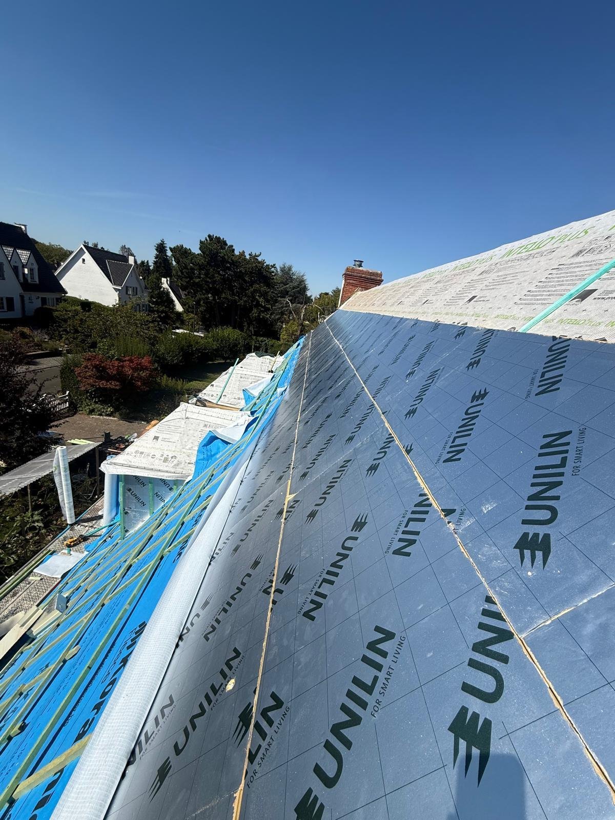 Residential roof under construction with waterproofing material, suburban houses in background