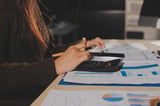 Person analyzing business charts and data using calculator at desk with financial reports