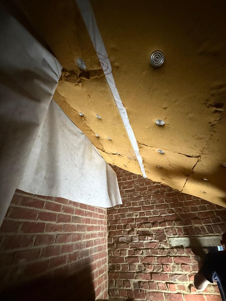 Water-stained ceiling with peeling paint, exposed brick walls, and metal ceiling fixtures in a damaged room interior