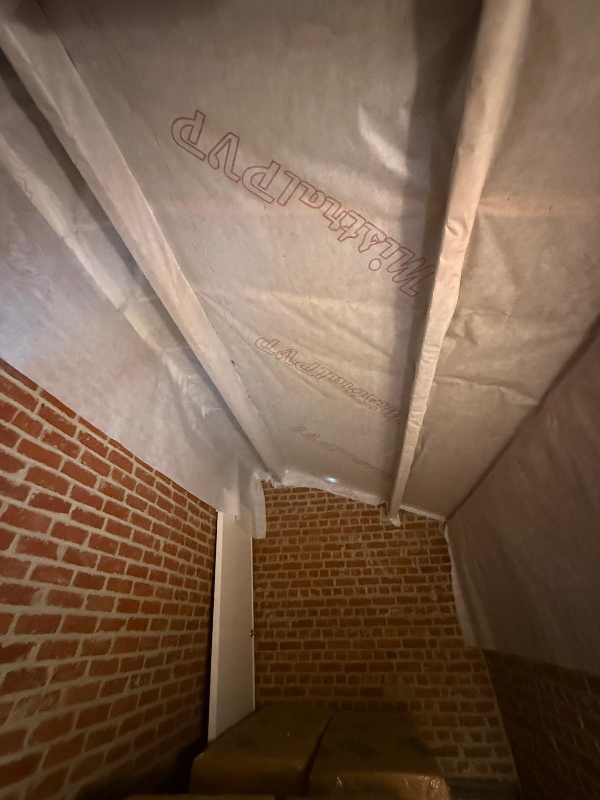 Interior corner of room with exposed red brick walls and white plastic sheeting taped overhead
