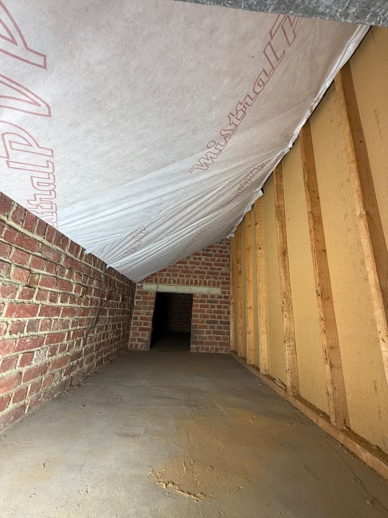 Empty basement or garage under construction with exposed brick walls, wooden framing, and plastic sheeting on ceiling